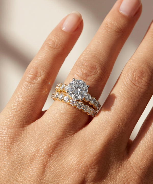 Close-up of a hand wearing two diamond rings on a neutral background