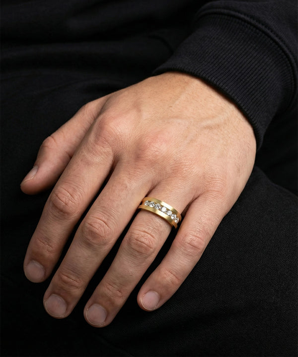 Hand wearing a gold ring with diamonds on a black background
