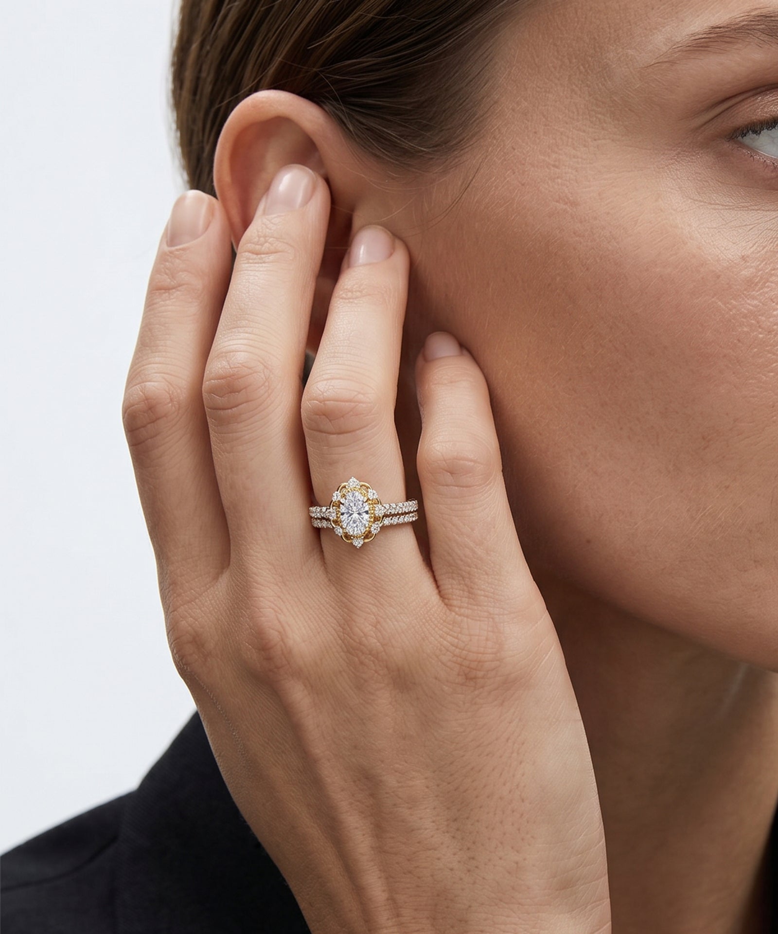 Close-up of a hand wearing a diamond ring, touching the ear against a neutral background
