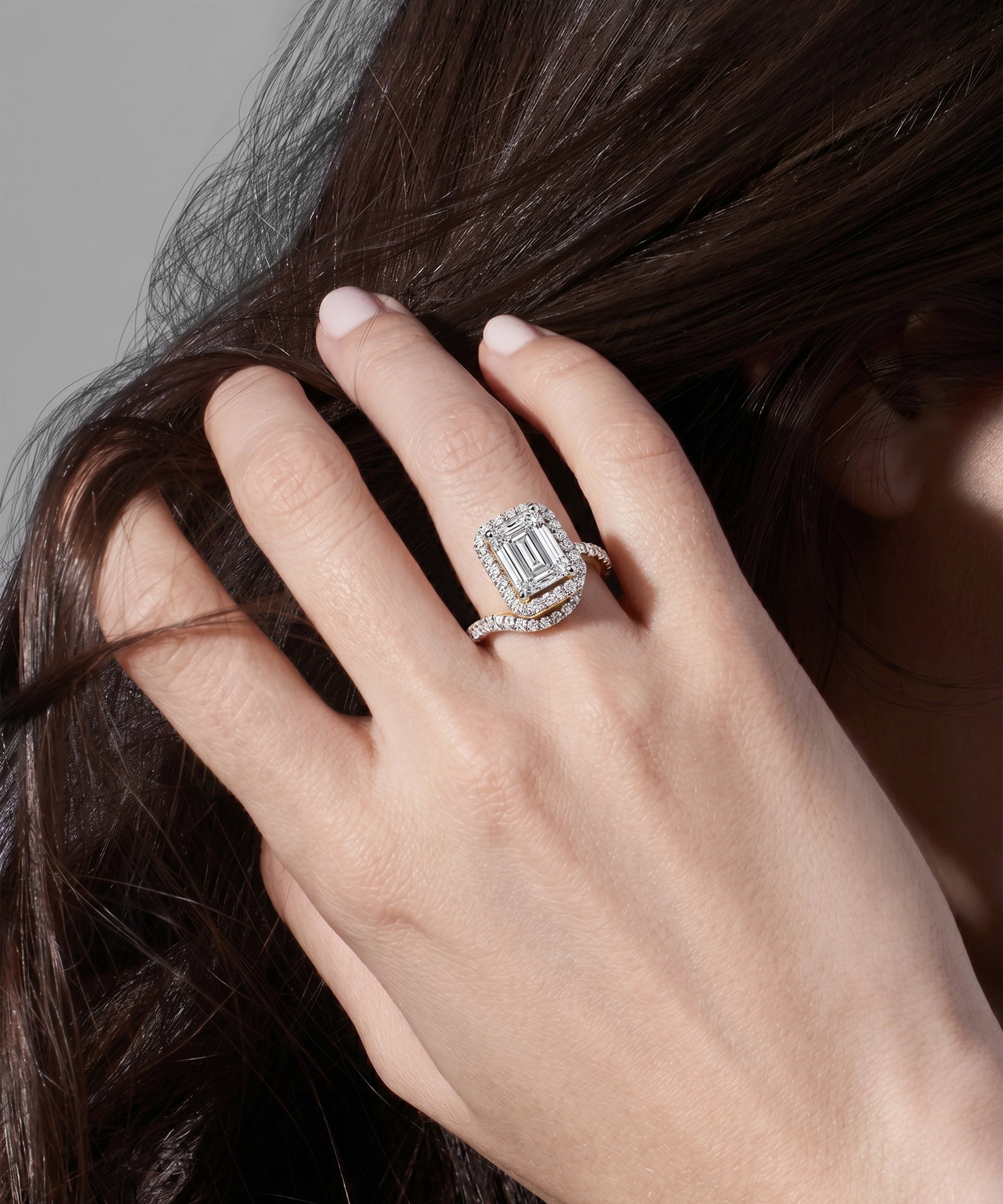 Hand with a diamond ring holding dark hair against a neutral background