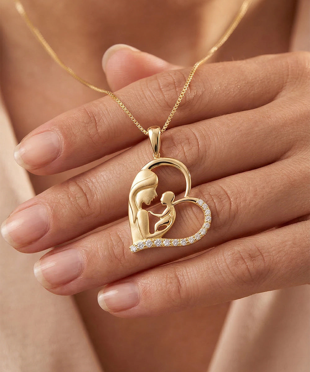 Gold necklace with a heart-shaped pendant featuring a mother and child design, held by a hand.