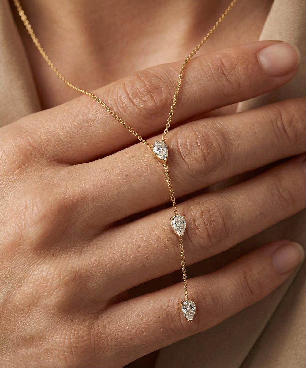 Gold necklace with heart-shaped pendants on a hand against a neutral background