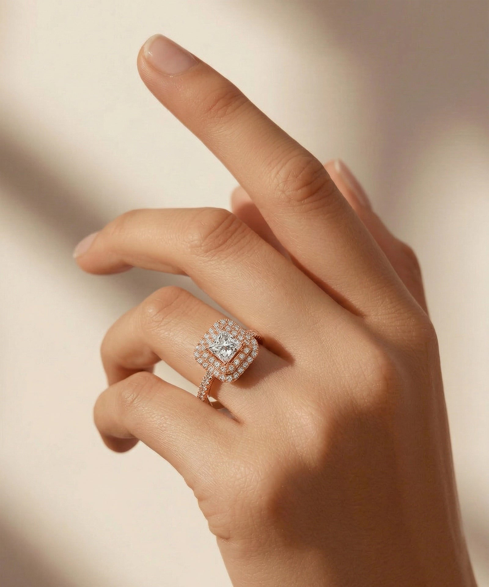 Hand wearing a diamond ring on a neutral background