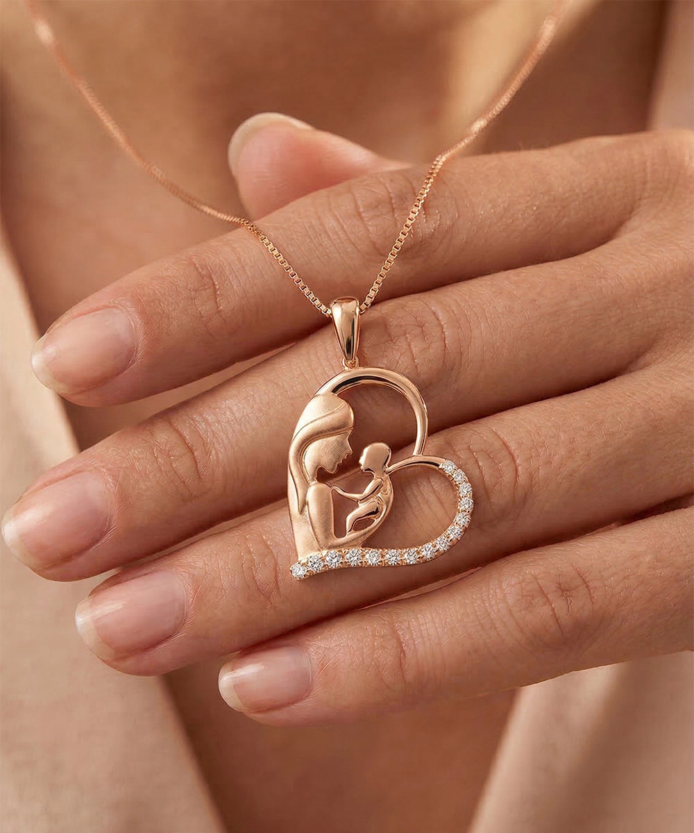 Rose gold necklace with heart-shaped pendant featuring a mother and child design held by a hand.