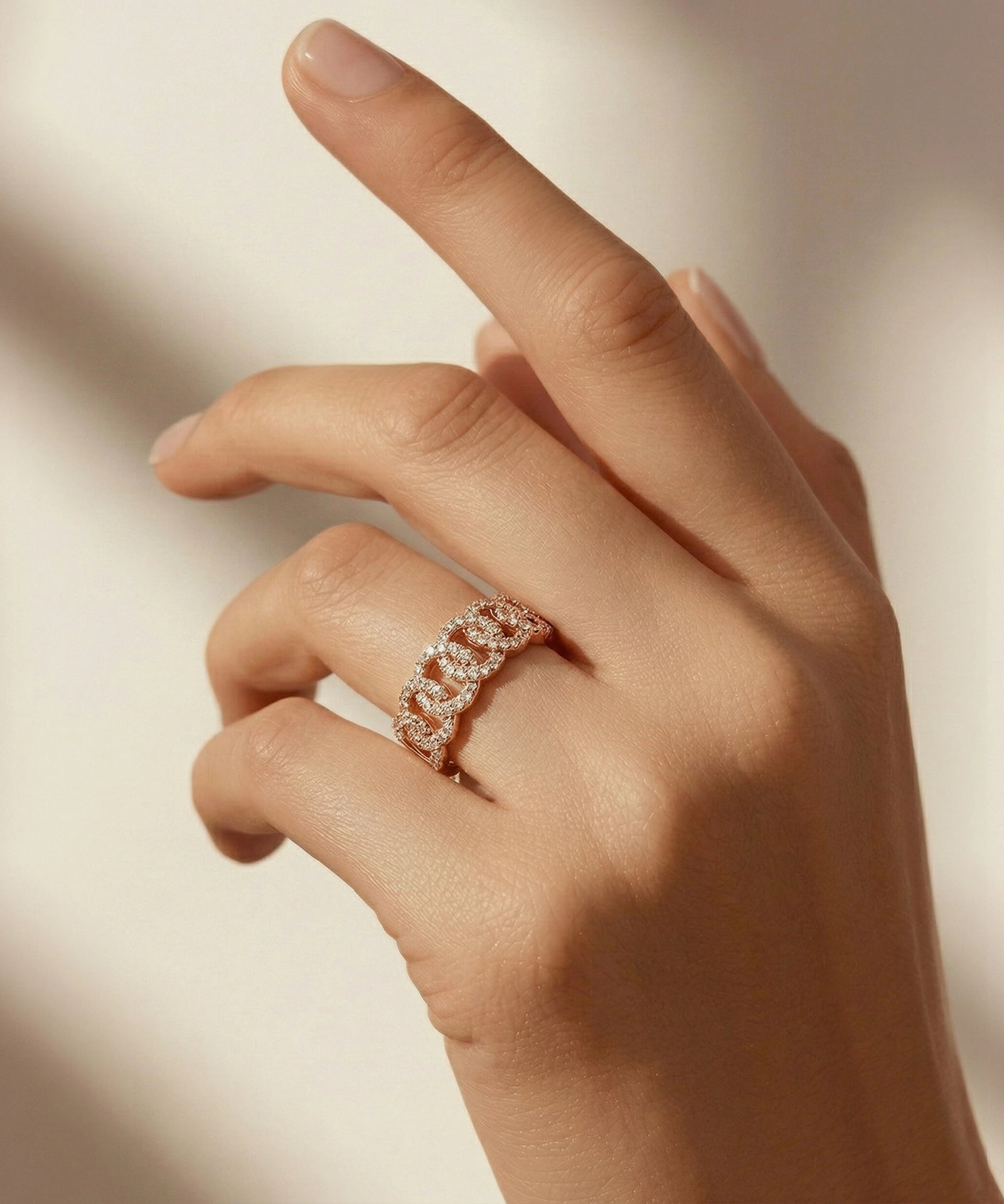 Hand wearing a rose gold ring with diamonds on a neutral background
