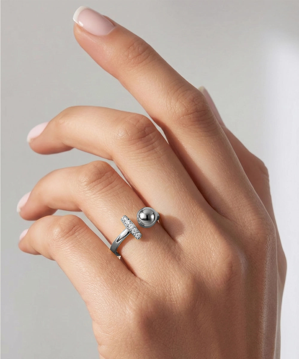 Hand wearing a silver ring with a large bead on a neutral background