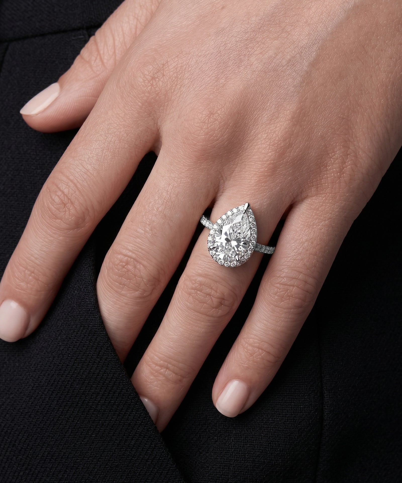 Close-up of a hand wearing a pear-shaped diamond ring on a black background