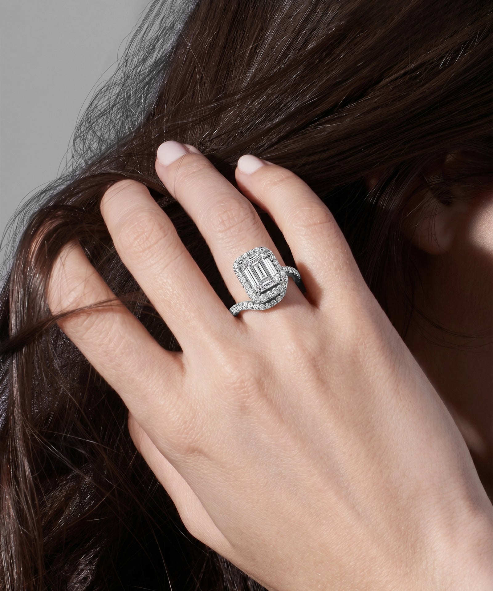 Hand with a diamond ring holding hair against a neutral background