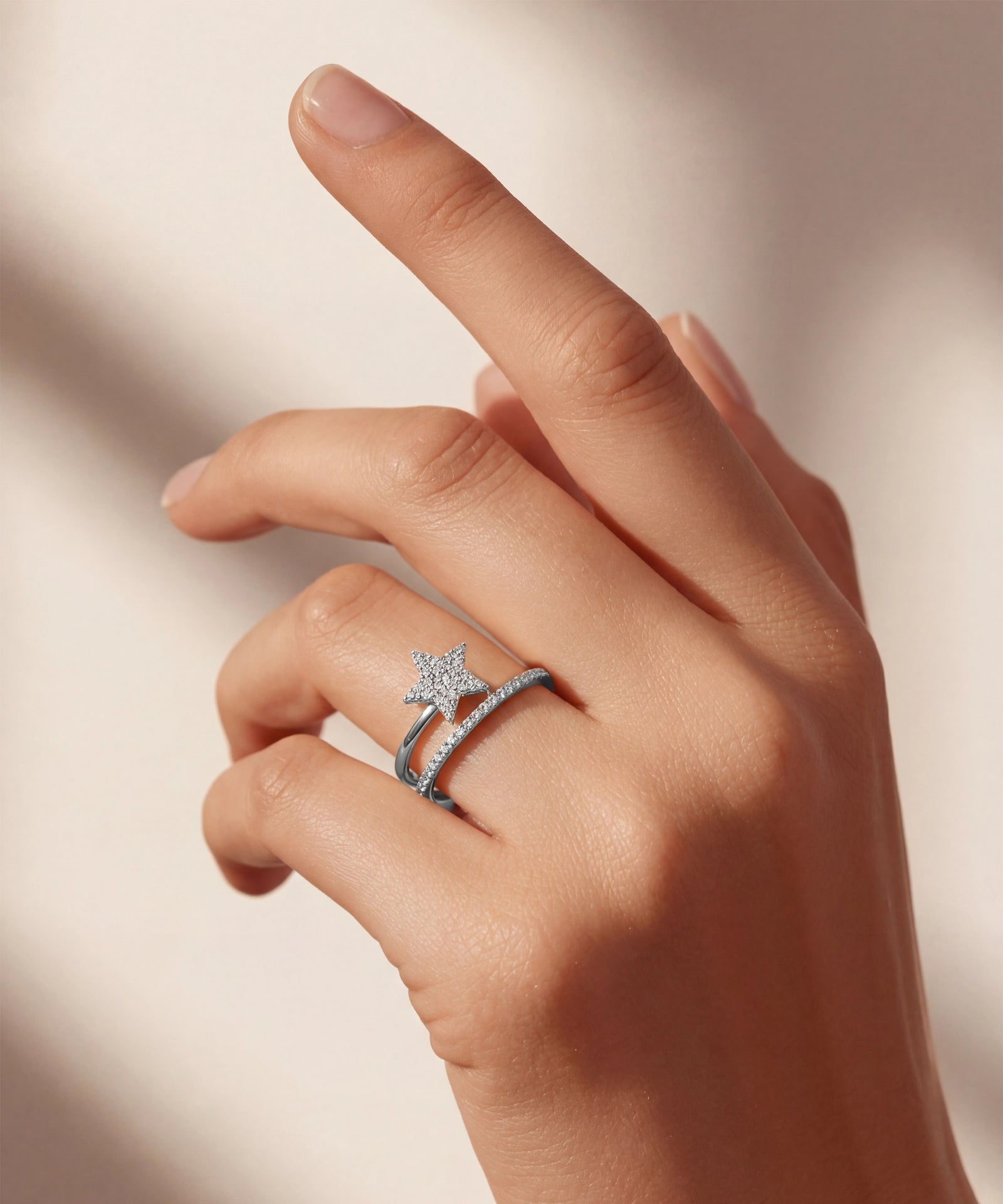 Hand wearing a silver ring with a star design on a neutral background