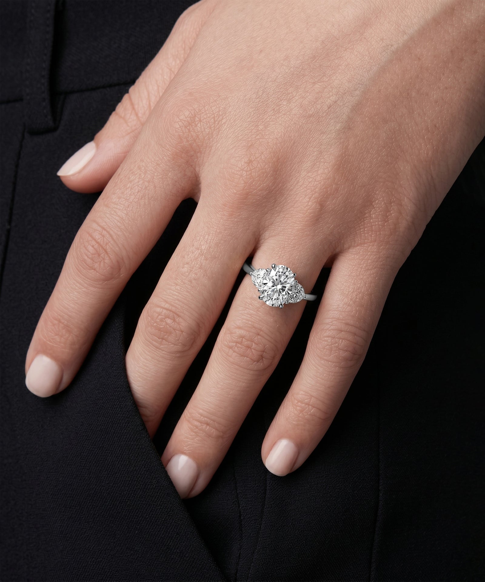 Hand wearing a diamond ring against a black background