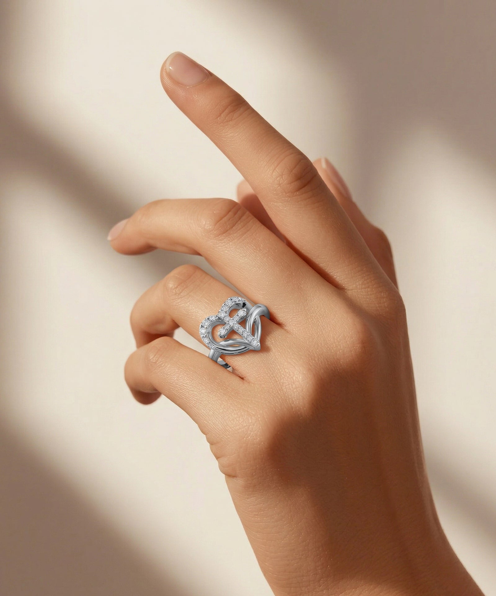 Hand wearing a silver heart-shaped ring on a neutral background
