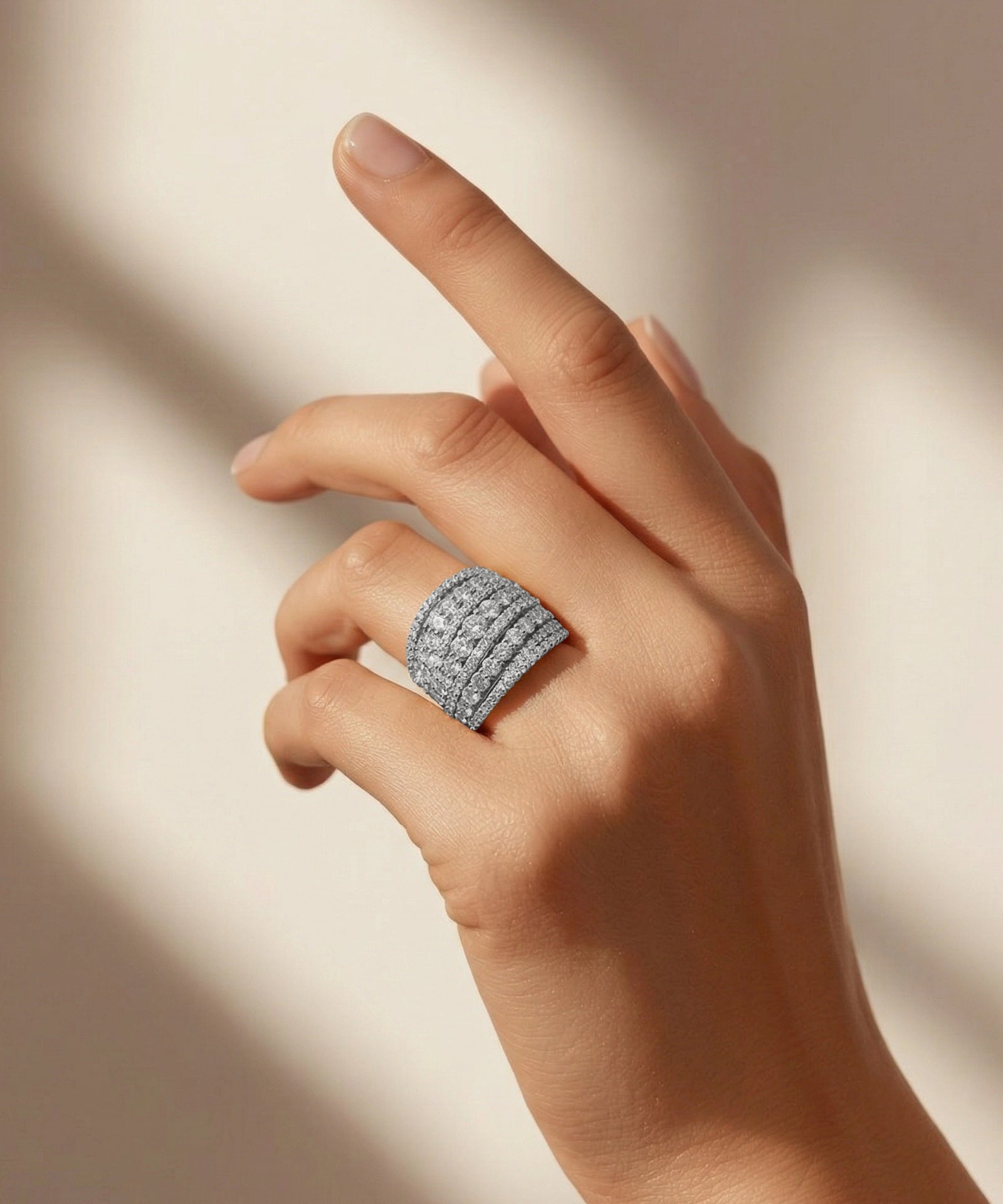 Hand wearing a silver ring with multiple diamonds on a neutral background