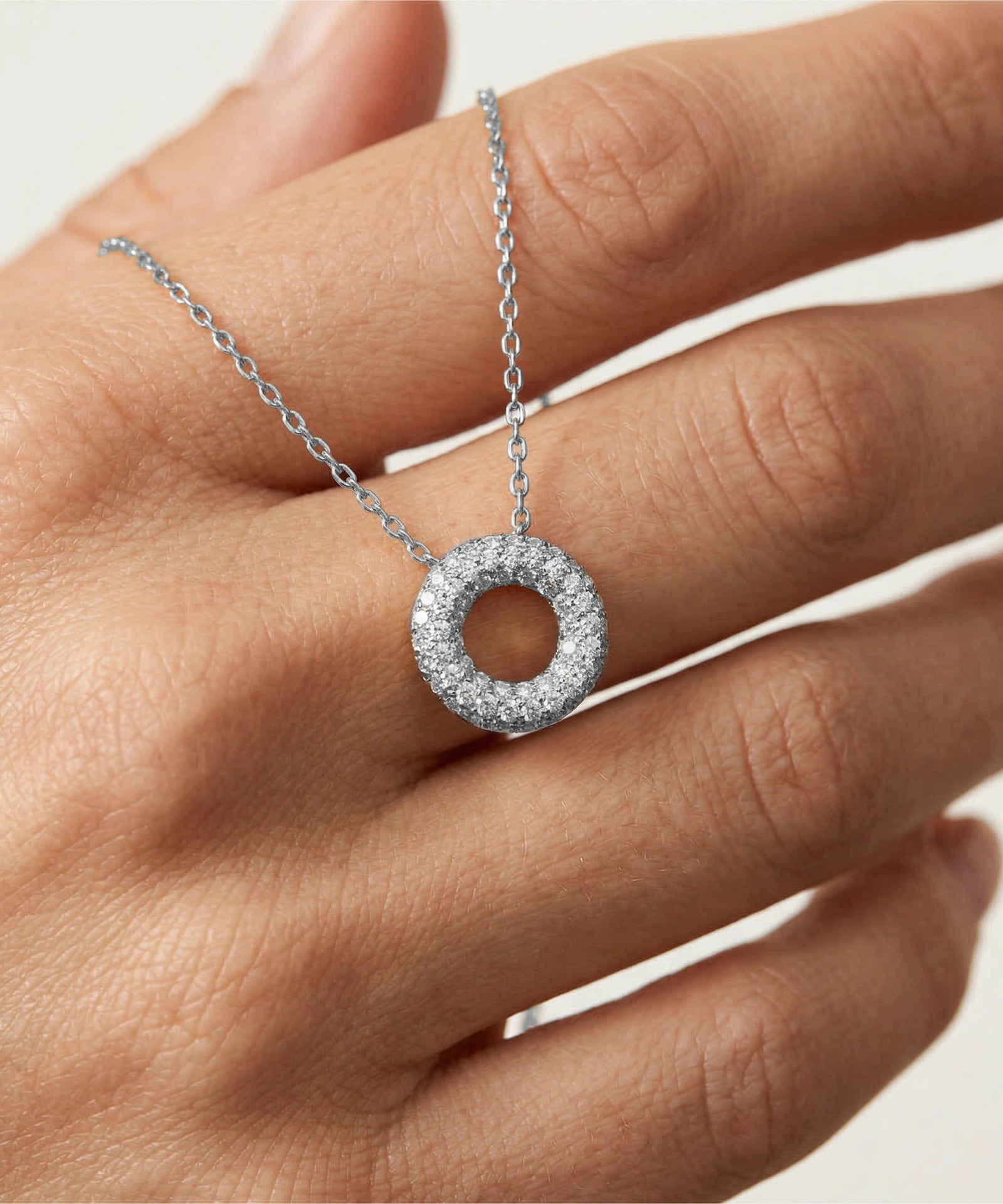 Silver necklace with a circular pendant on a hand against a neutral background