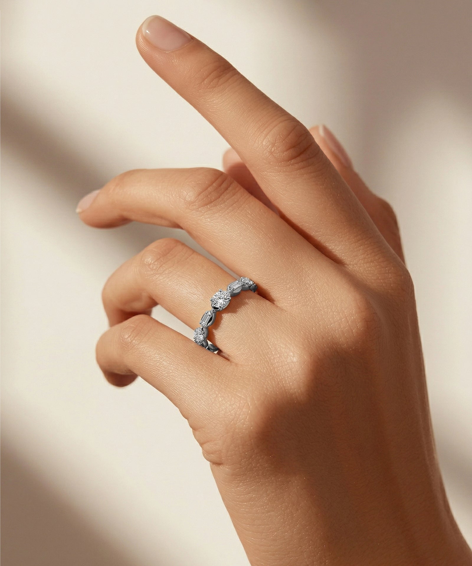 Hand wearing a silver ring on a neutral background