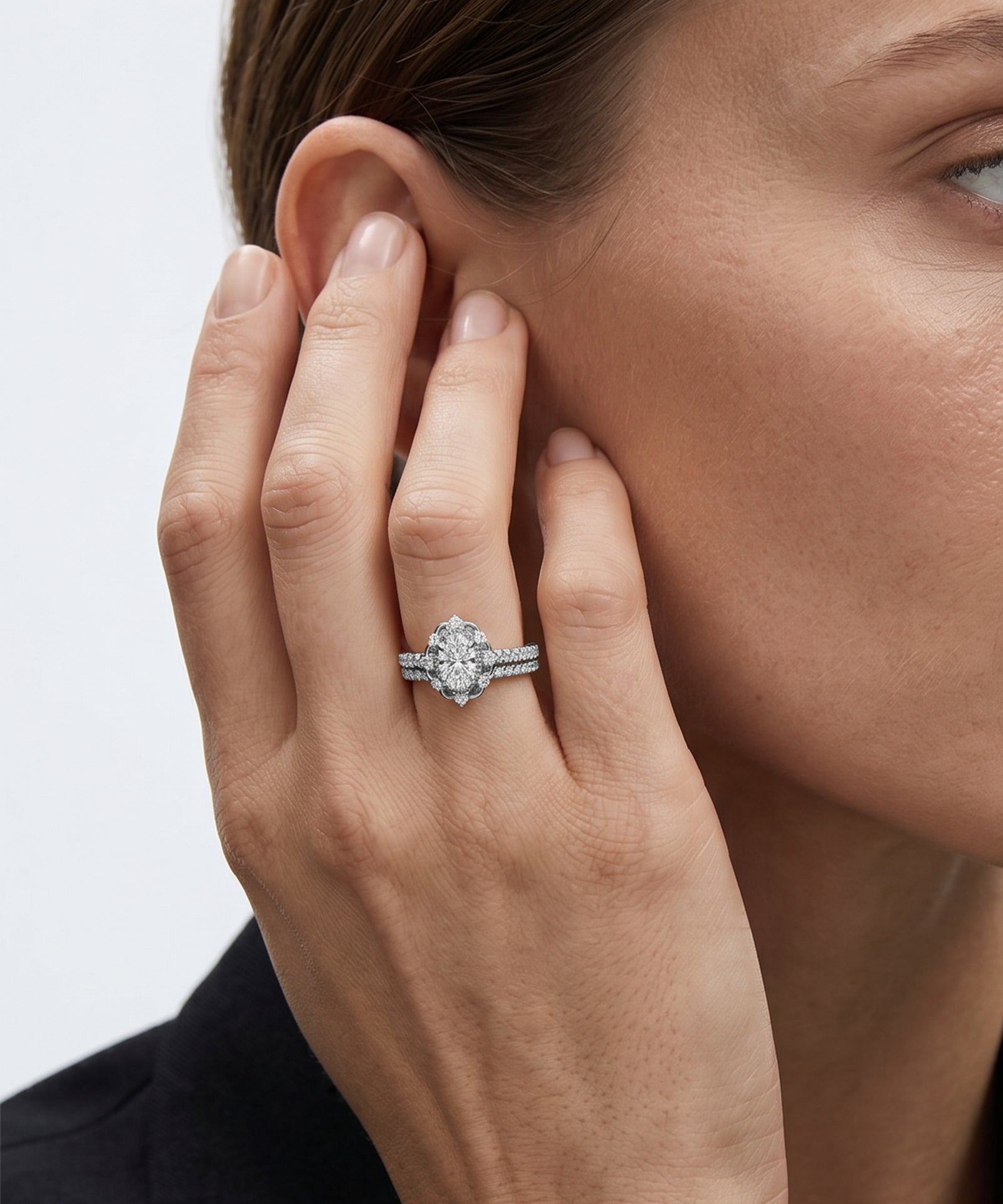 Close-up of a hand wearing a diamond ring, touching the ear against a neutral background