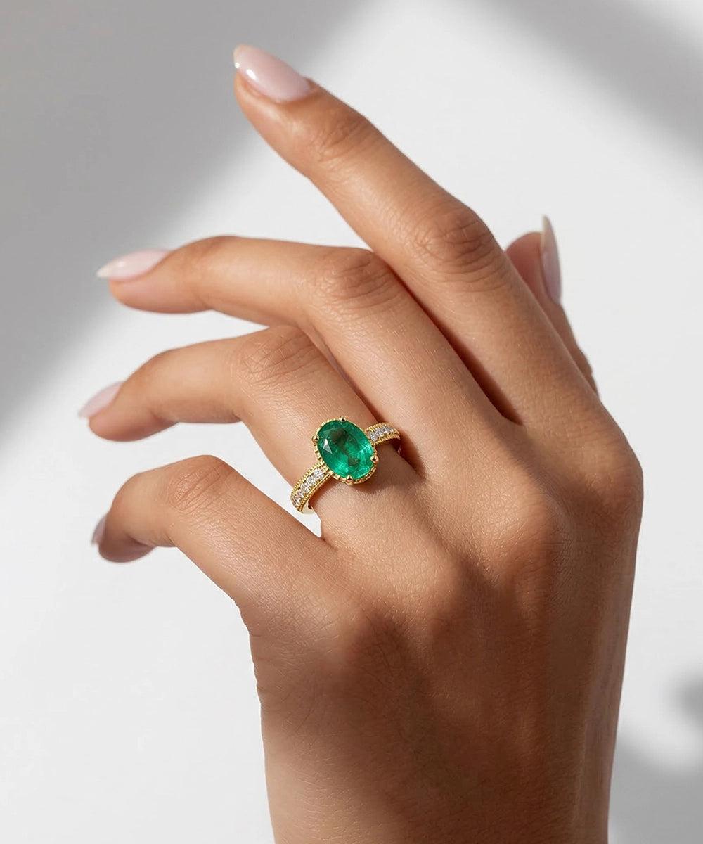 Hand wearing a ring with a green gemstone on a neutral background