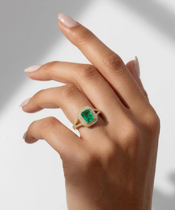 Hand wearing a ring with a green gemstone on a neutral background