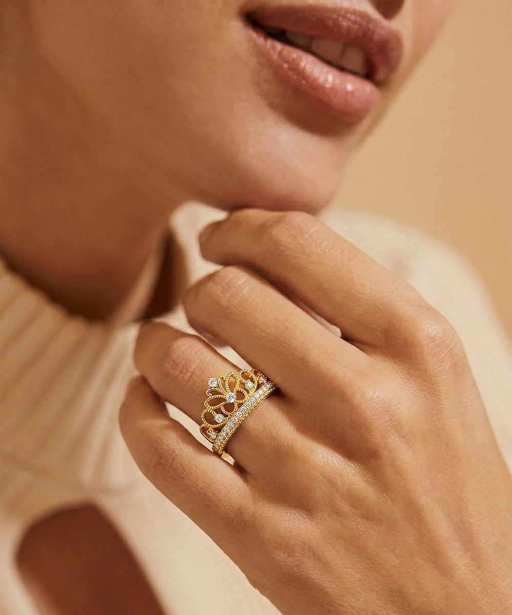 Close-up of a hand wearing a gold ring with diamonds, against a neutral background.