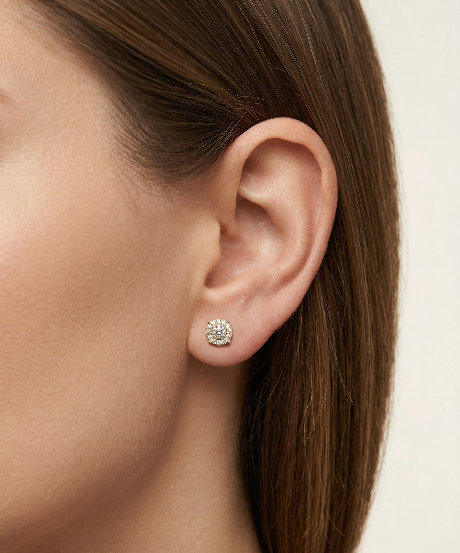 Close-up of a person wearing a diamond stud earring on a neutral background