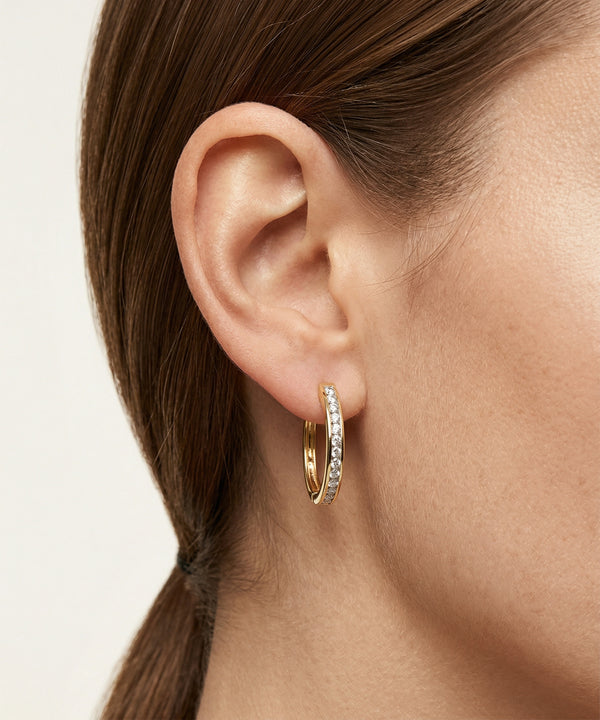 Gold hoop earrings worn by a person with a neutral background