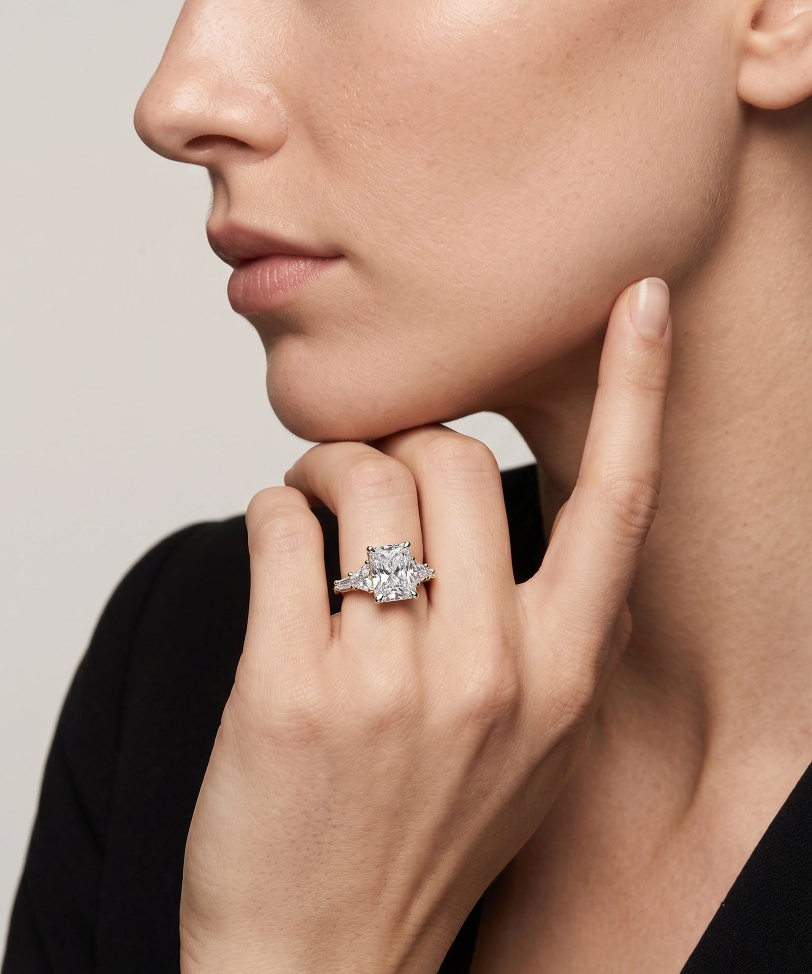 Close-up of a hand wearing a diamond ring on a neutral background