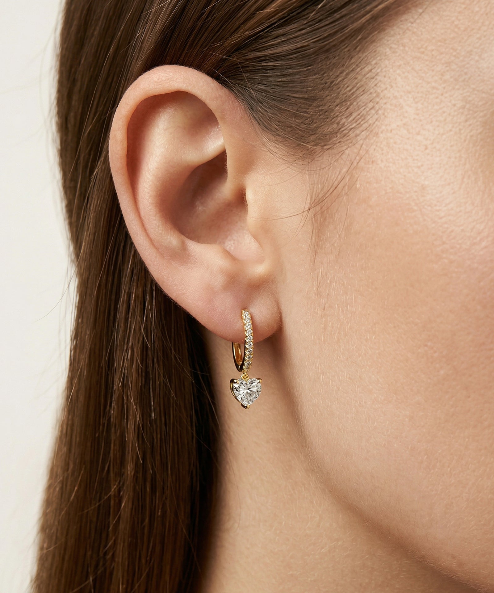 Close-up of an ear wearing a heart-shaped earring with a plain background