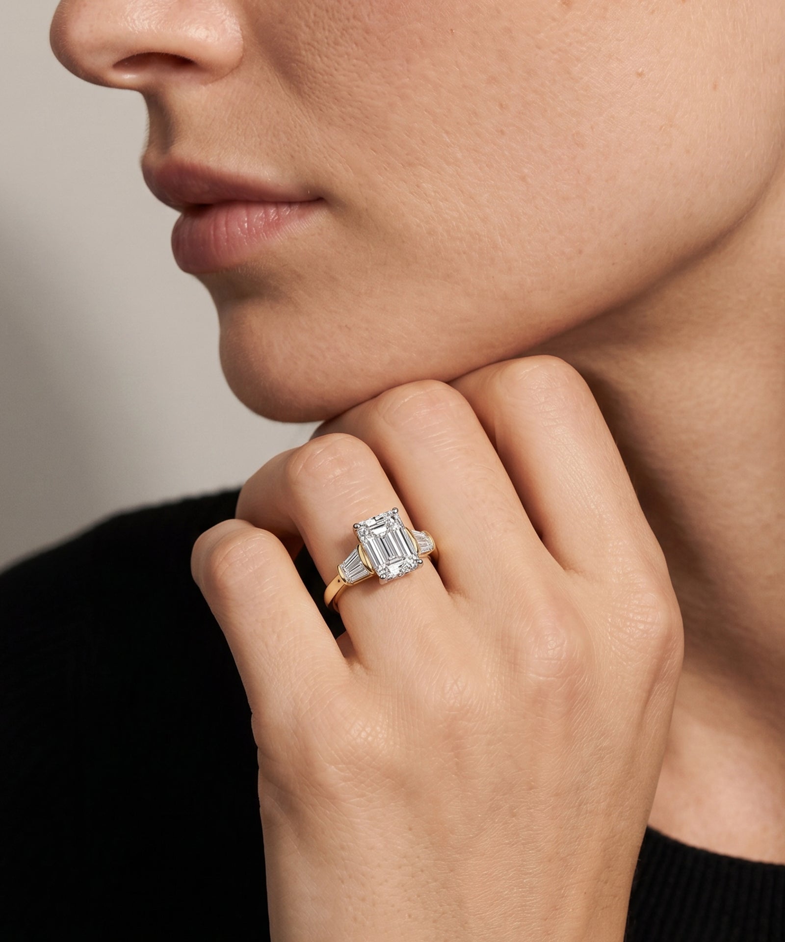 Close-up of a hand wearing an emerald-cut diamond ring against a neutral background