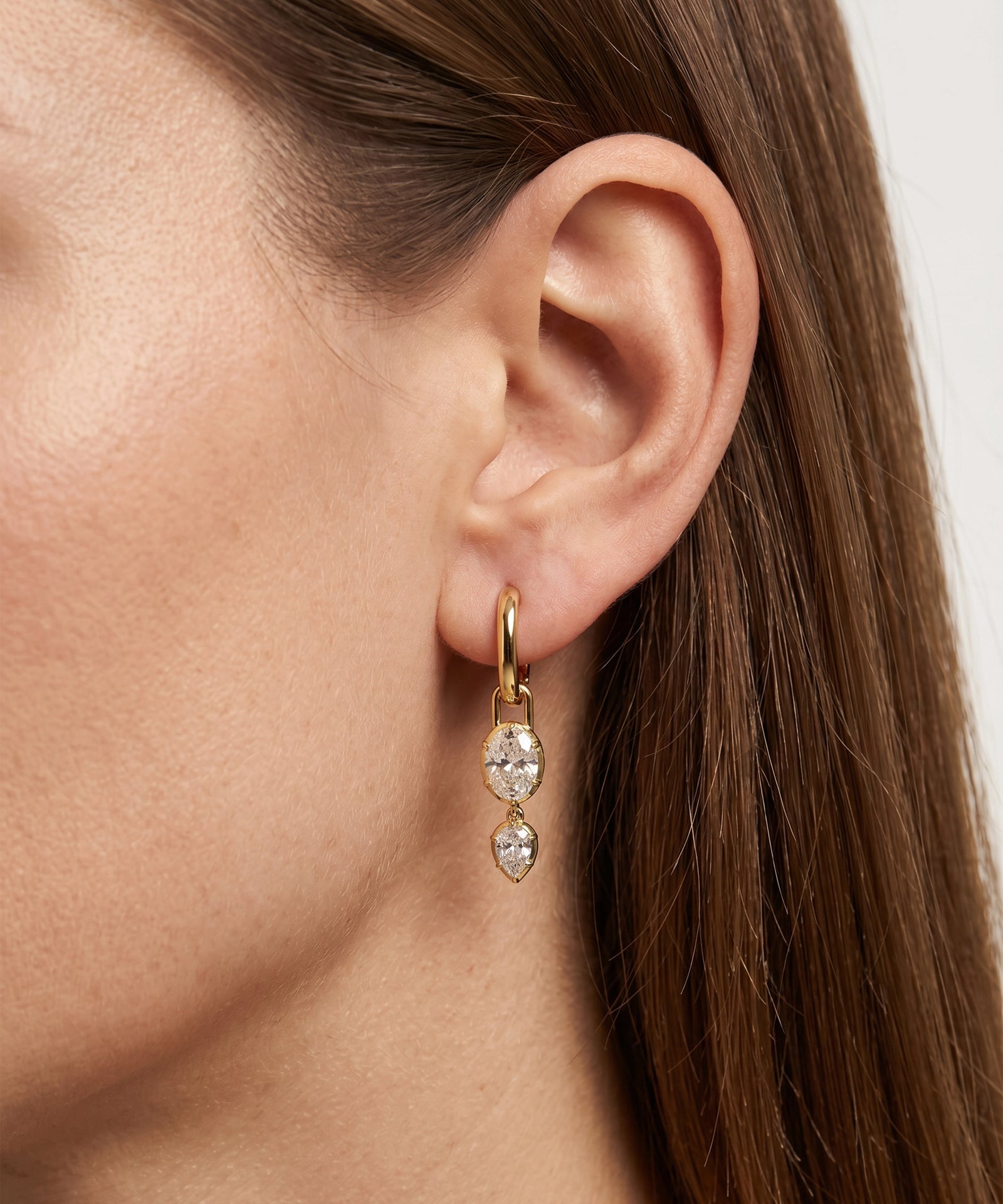 Close-up of a person wearing gold hoop earrings with clear gemstones.