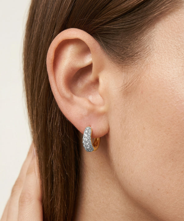 Close-up of an ear wearing a diamond earring with a neutral background