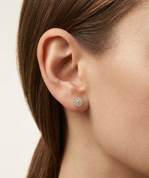 Close-up of an ear wearing a diamond stud earring on a neutral background
