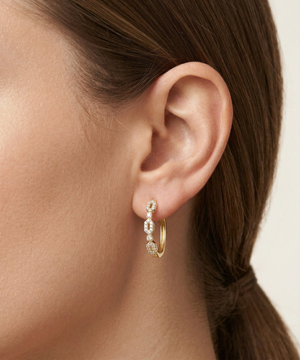 Close-up of an ear wearing gold hoop earrings with small diamonds.