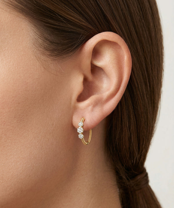 Close-up of an ear wearing a gold hoop earring with small stones.