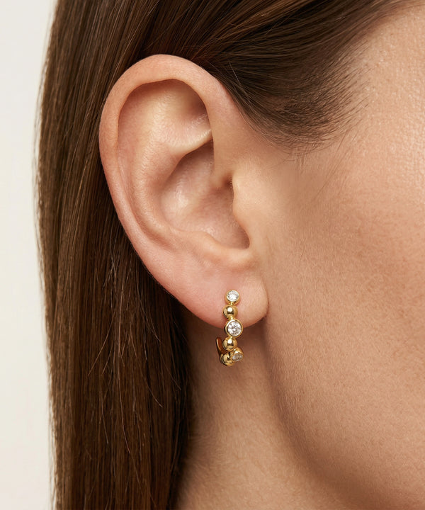 Close-up of an ear wearing gold hoop earrings with a neutral background