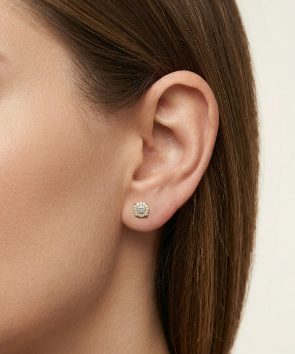 Close-up of an ear wearing a diamond stud earring with a neutral background