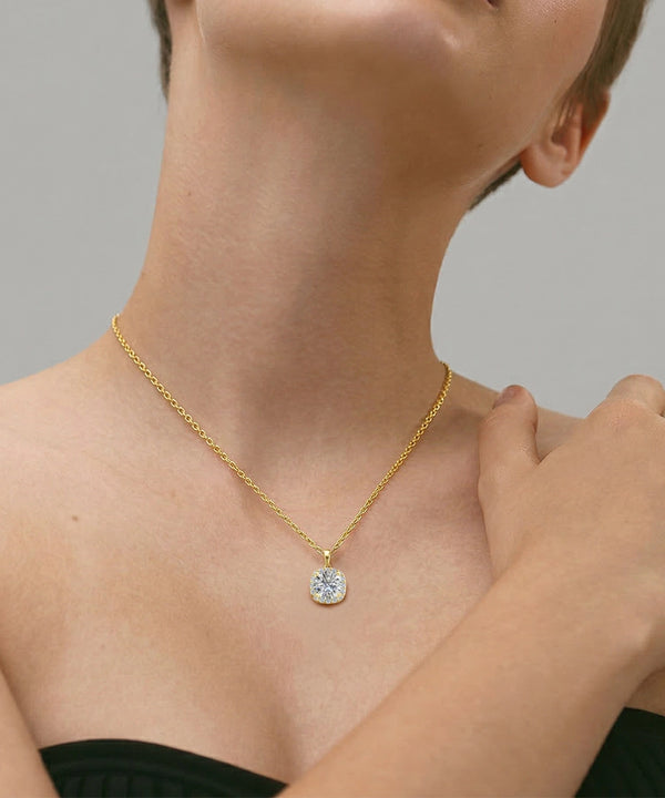 Gold necklace with a pendant on a person against a neutral background