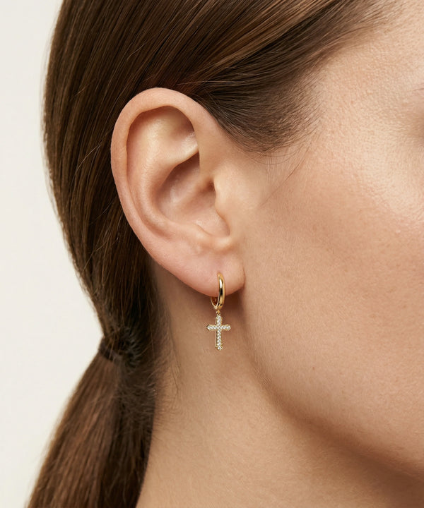 Gold cross earring worn by a person with a neutral background