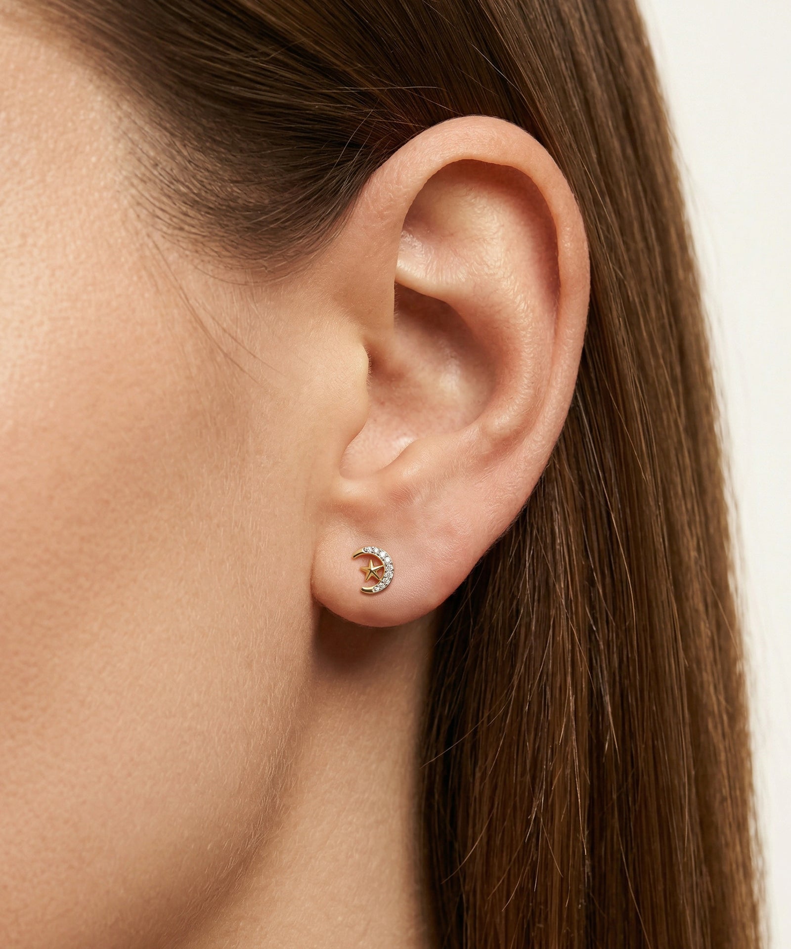 Close-up of an ear wearing a gold earring with a small round design.
