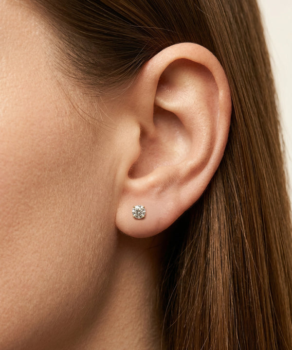 Close-up of an ear wearing a diamond stud earring with a neutral background
