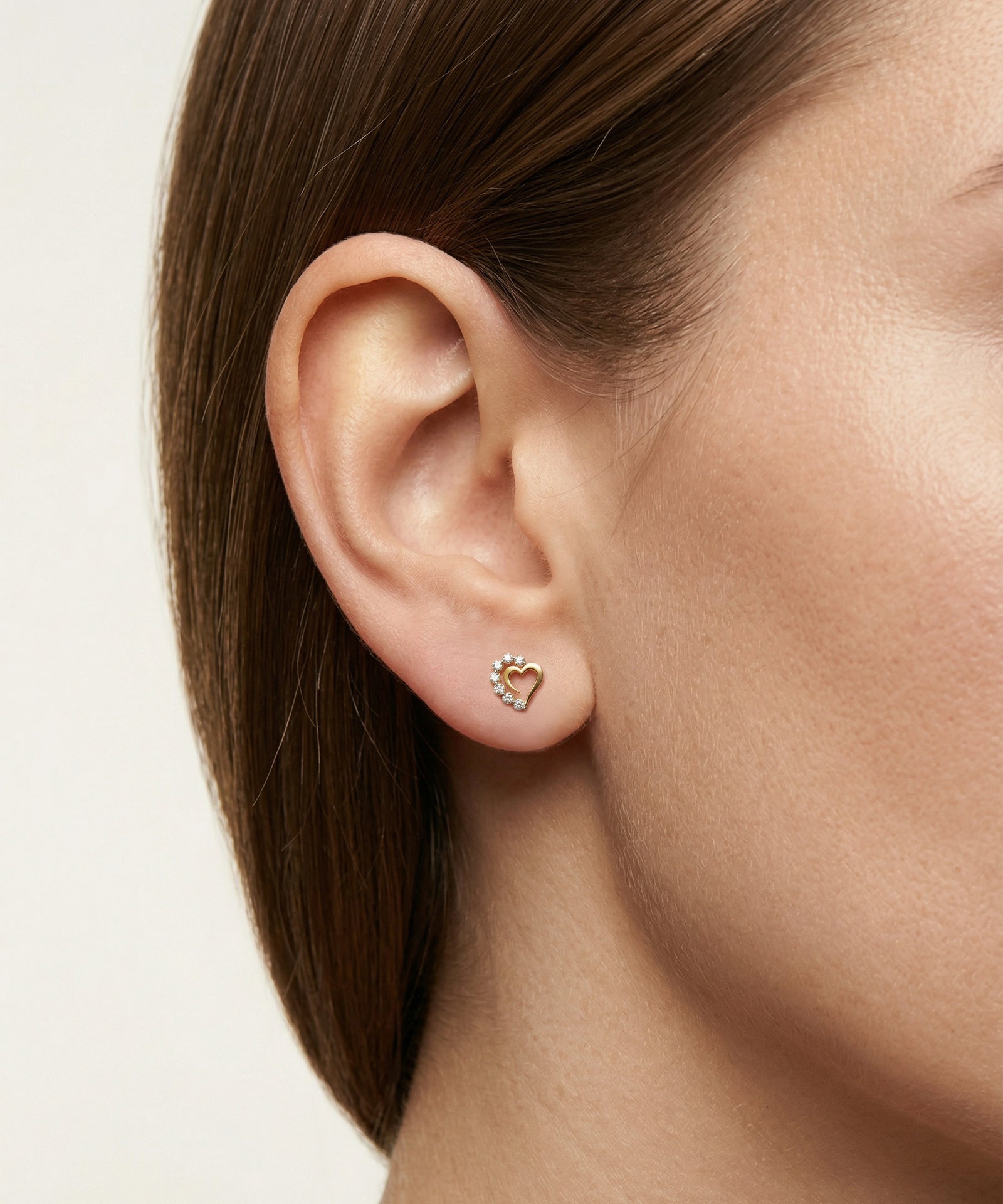 Close-up of an ear wearing a heart-shaped earring on a neutral background