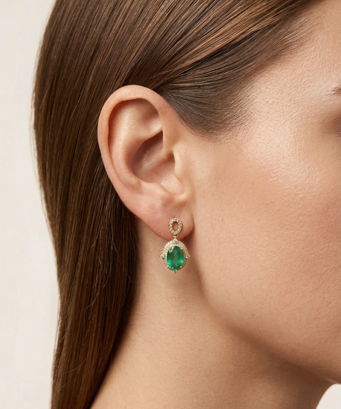Close-up of a person wearing emerald green earrings with gold accents.