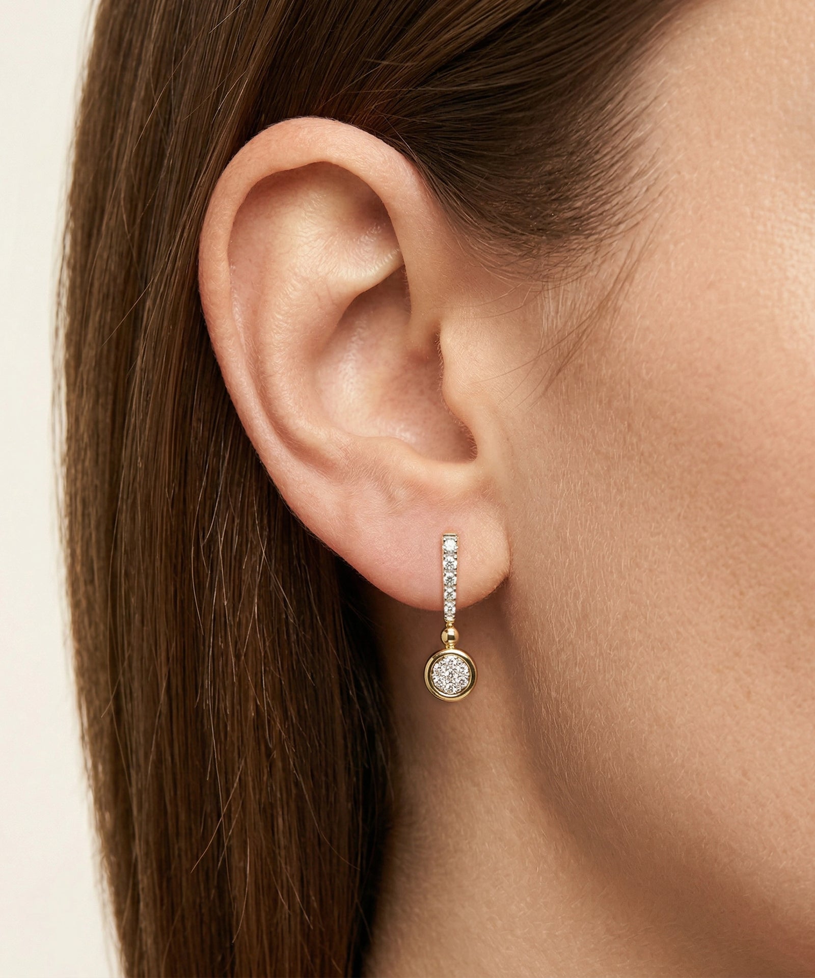 Close-up of an ear wearing a gold earring with a clear gemstone.