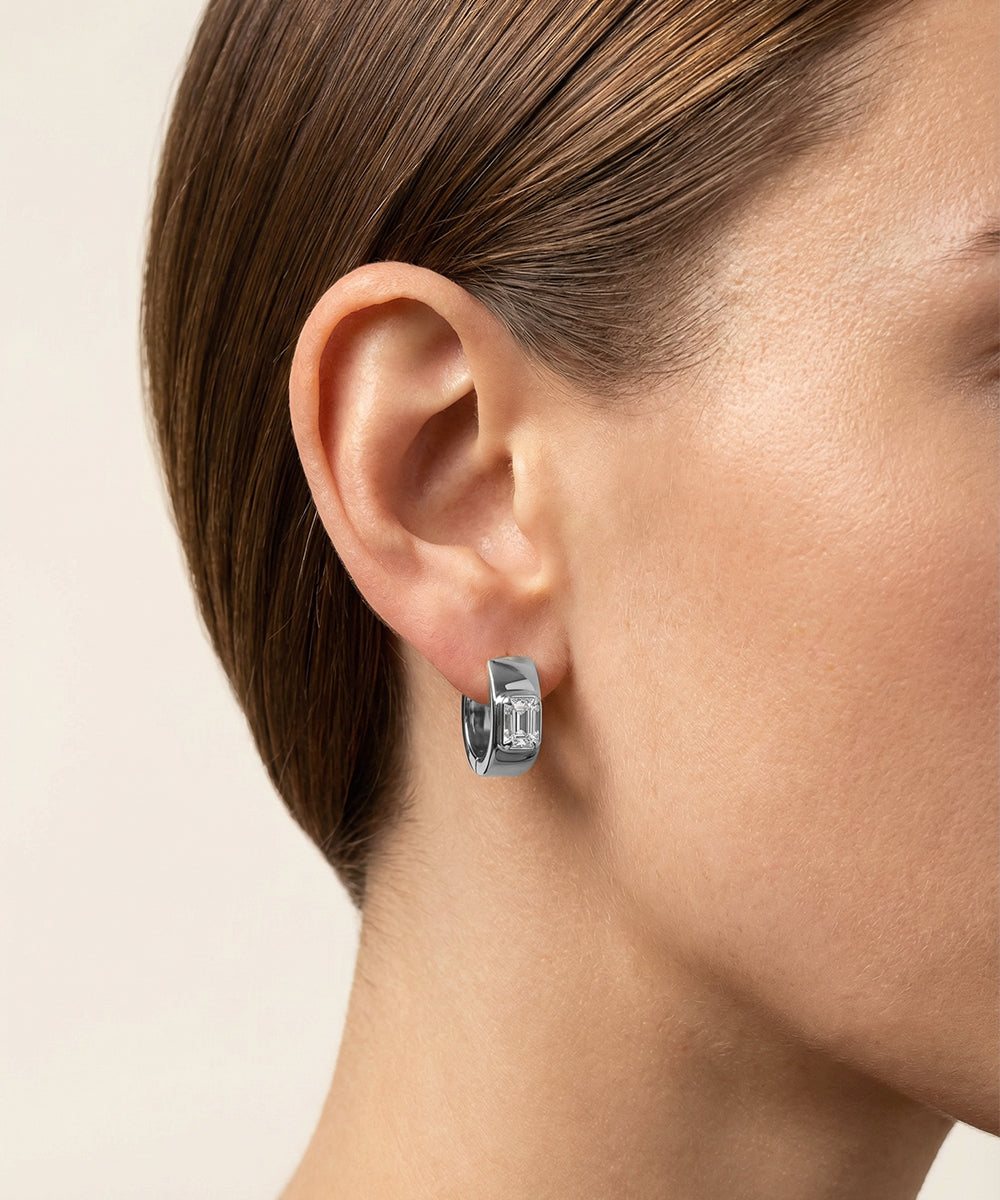 Close-up of a person wearing silver hoop earrings with a neutral background