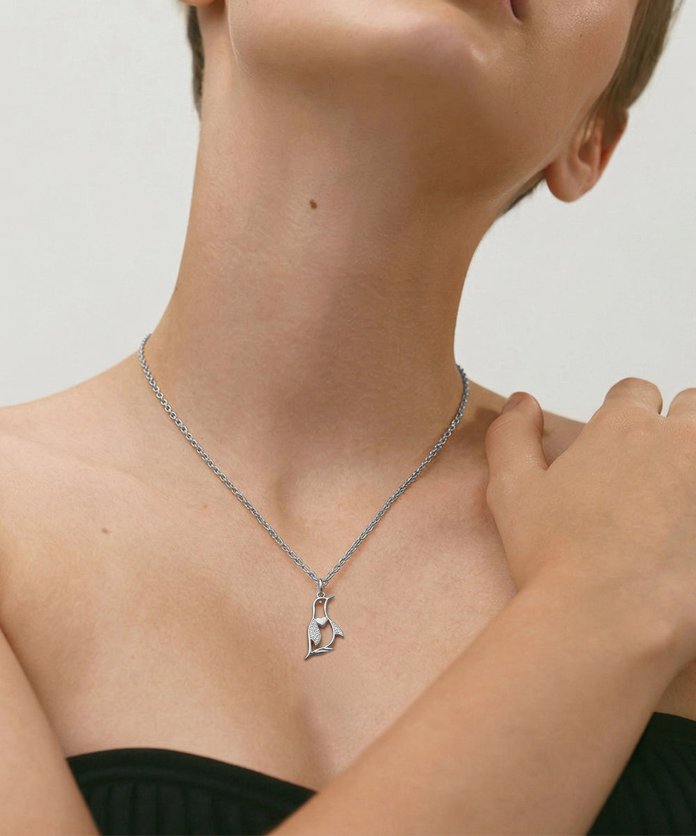 Person wearing a silver necklace with a pendant on a plain background