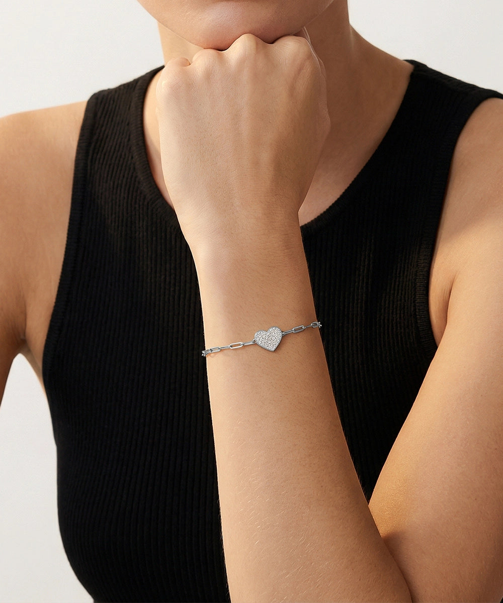 Silver bracelet with heart charm on a person's wrist against a neutral background