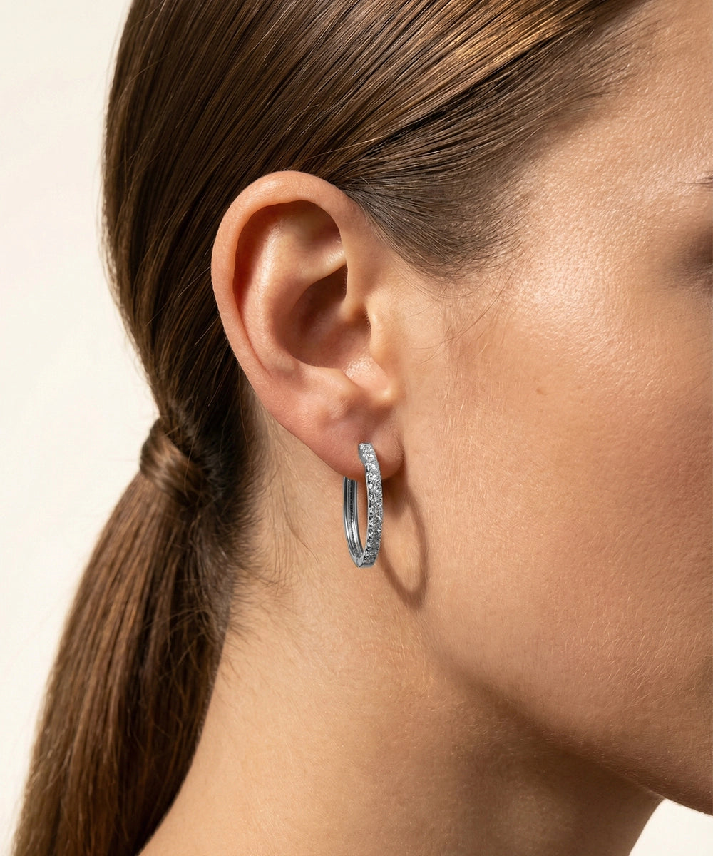 Close-up of a person wearing gold hoop earrings with a neutral background