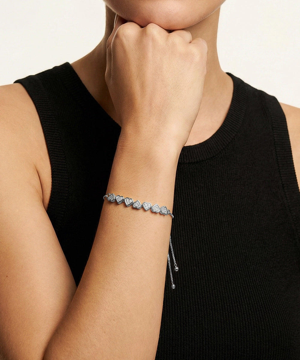Person wearing a bracelet with heart-shaped charms on a plain background