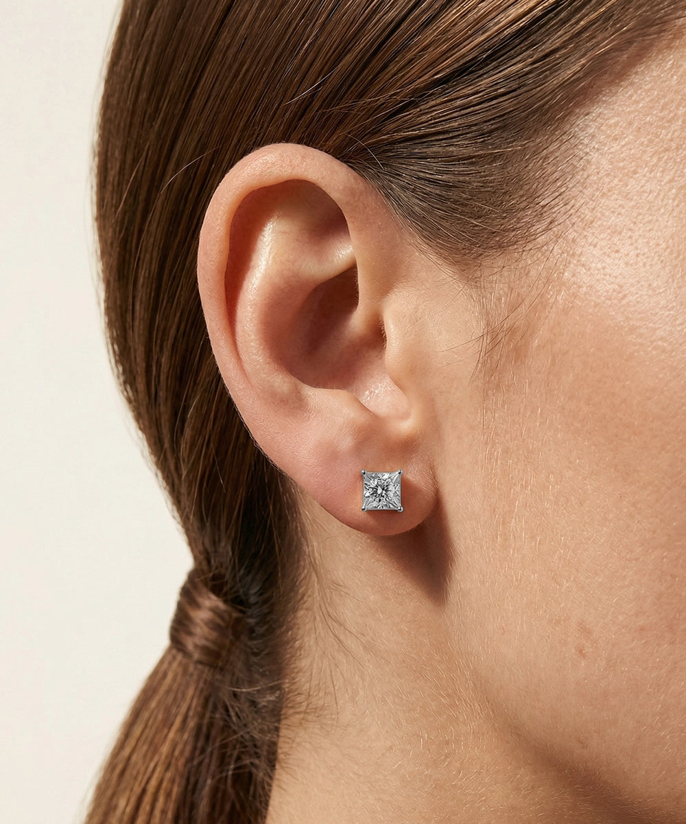 Close-up of an ear wearing a square diamond earring on a neutral background
