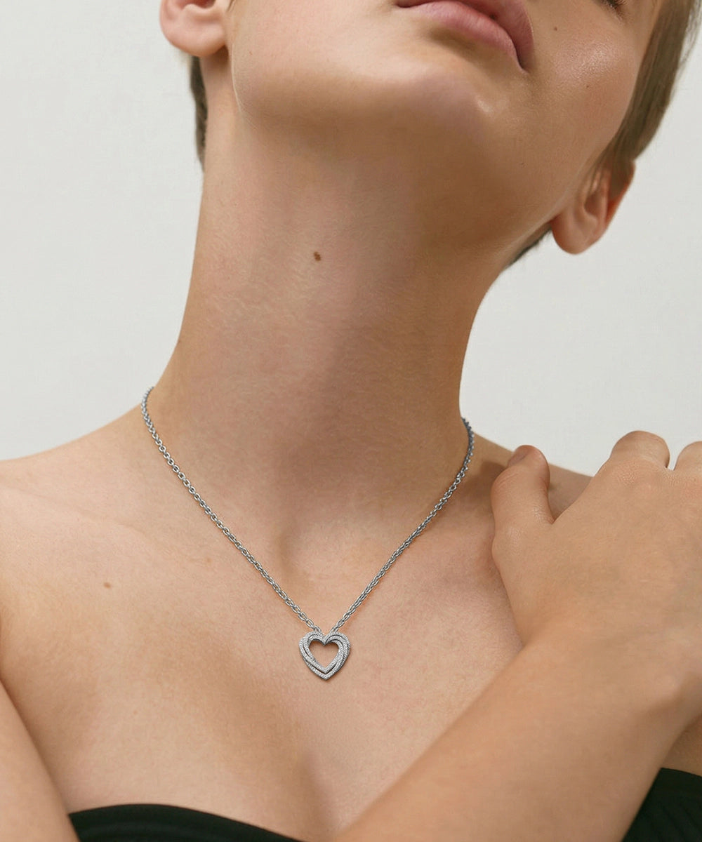 Person wearing a silver necklace with a heart pendant on a neutral background