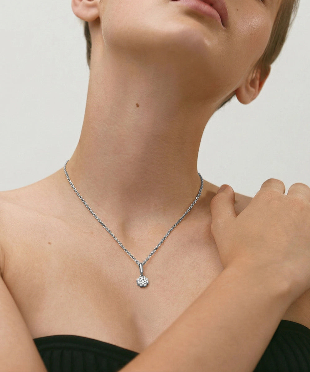 Person wearing a silver necklace with a small pendant on a neutral background