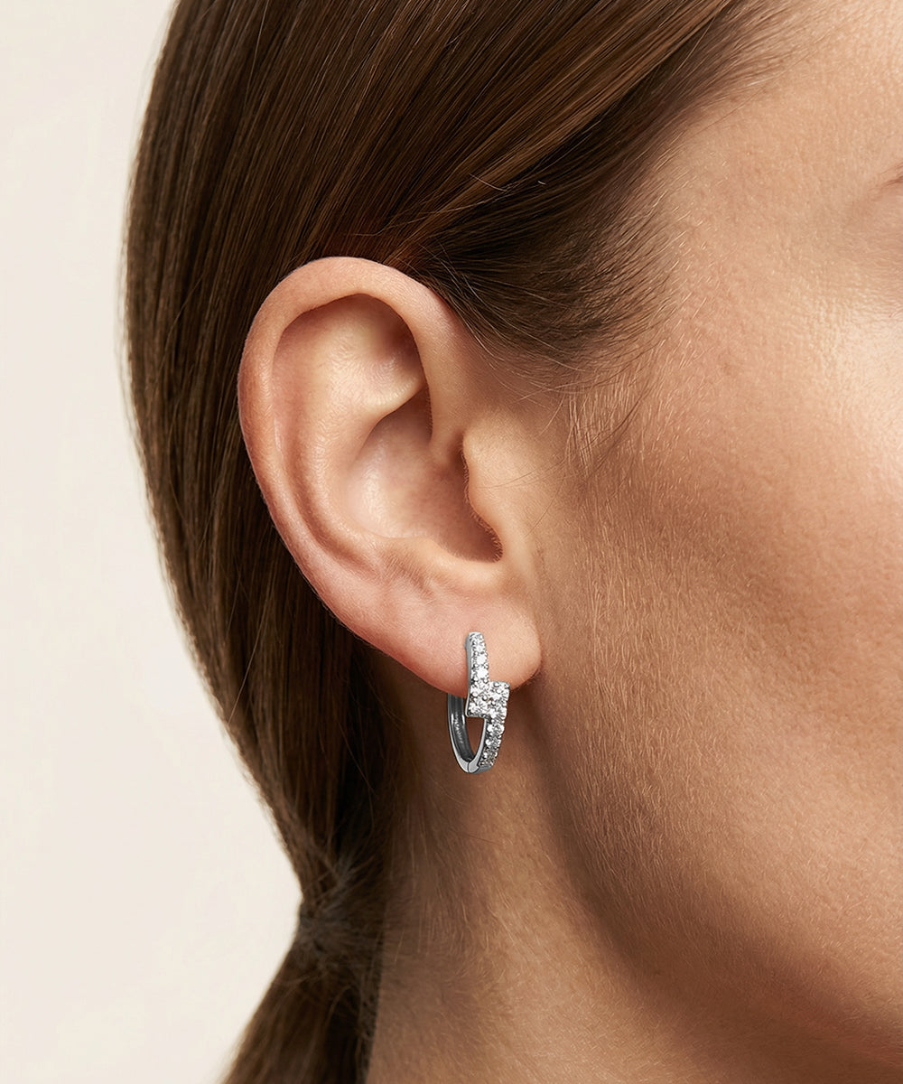 Close-up of an ear wearing a silver hoop earring on a neutral background